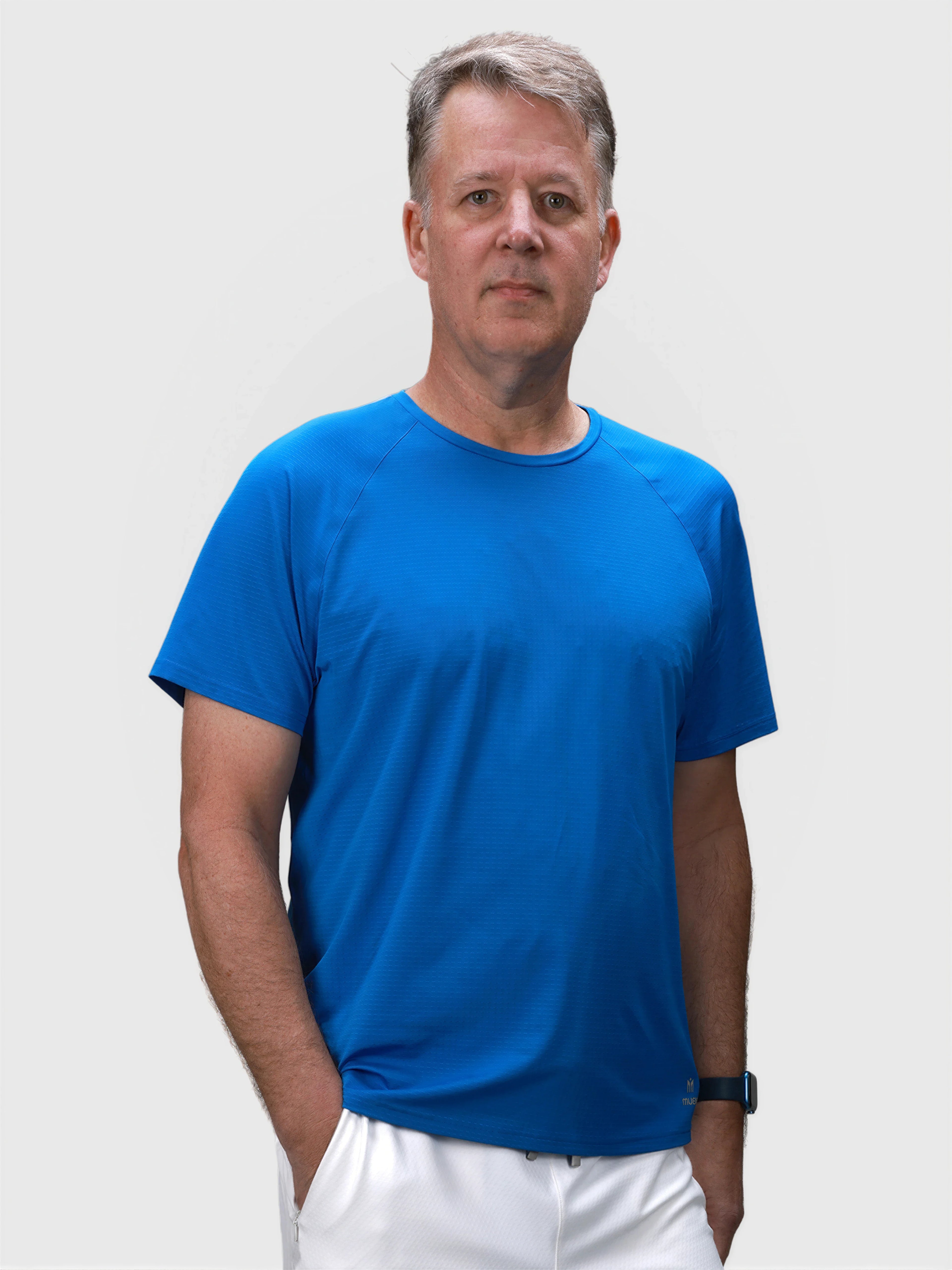 Man wearing blue Dink Performance tee paired with white shorts in pickleball clothing collection by MUEV
